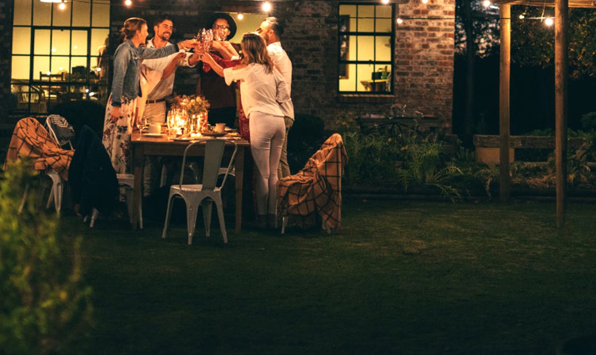 Friends toasting at a backyard dinner after dark, bugs kept away by a GOOTOP lantern